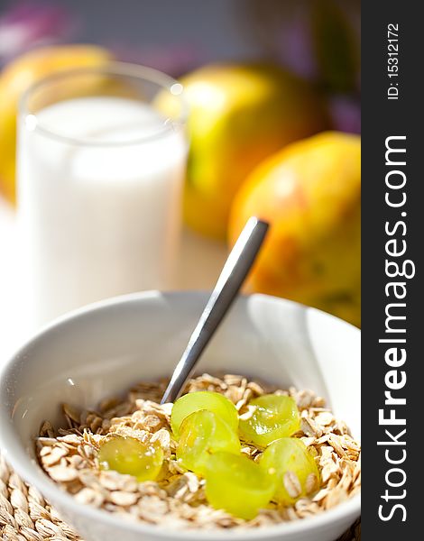 Muesli with oats in a white bowl on a table and milk in a glass in background. Muesli with oats in a white bowl on a table and milk in a glass in background