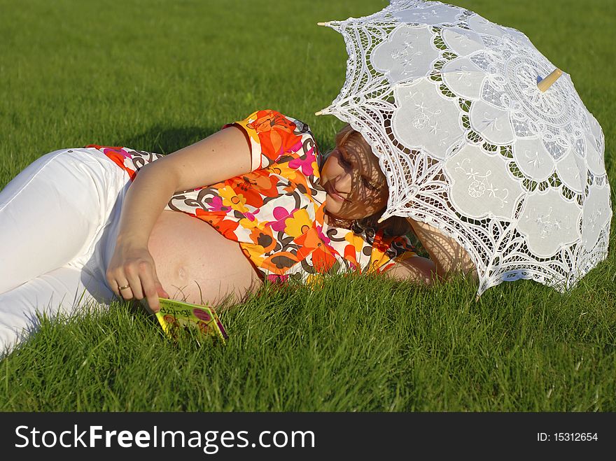 Pregnant woman lying on the grass, reading the small book