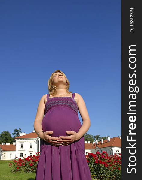 Pregnant woman with hands on the belly in the garden in front of the palace