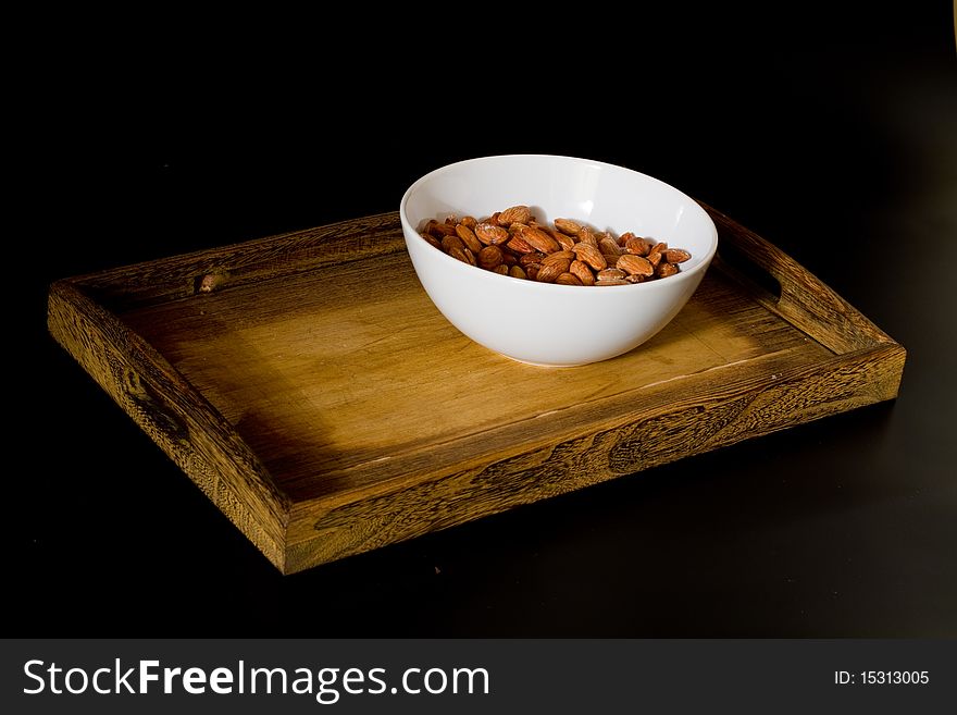 Bowl with almonds on wooden tray isolated on black background