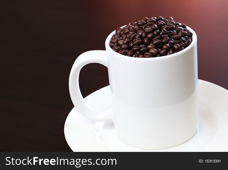 White Coffee mug filled with fresh coffee beans on dark background