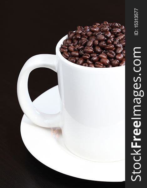 White Coffee mug filled with fresh coffee beans on dark background