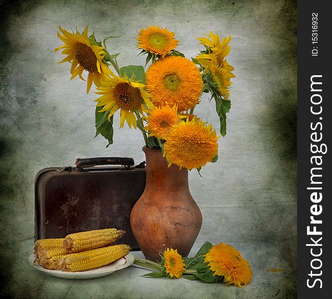 The bouquet of sunflowers stands in a jug, alongside old suitcase and boiled corn. The bouquet of sunflowers stands in a jug, alongside old suitcase and boiled corn