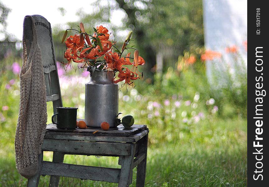 A bouquet of tiger lilies is in a can, a can stands on an old chair. A bouquet of tiger lilies is in a can, a can stands on an old chair.