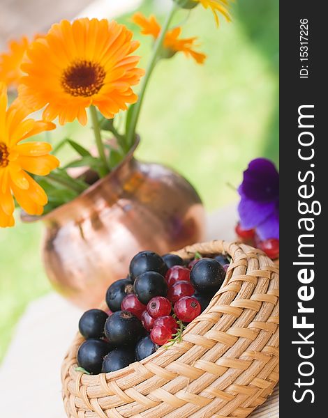 Black and red currant in a basket and a calendula bouquet