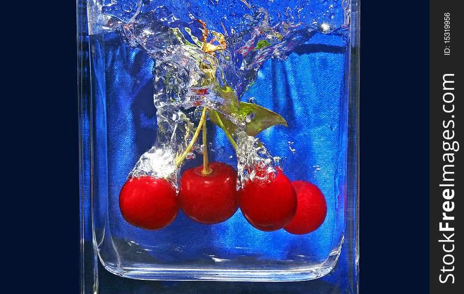 Ripe cherries fall in a glass with water