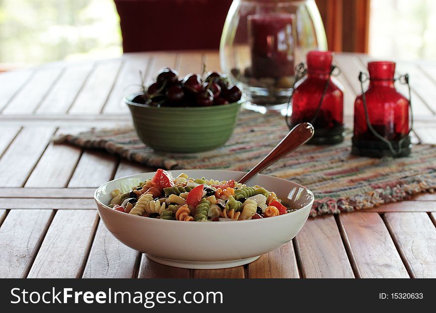 A teak wood table with fresh summer cherries and pasta salad. A teak wood table with fresh summer cherries and pasta salad.