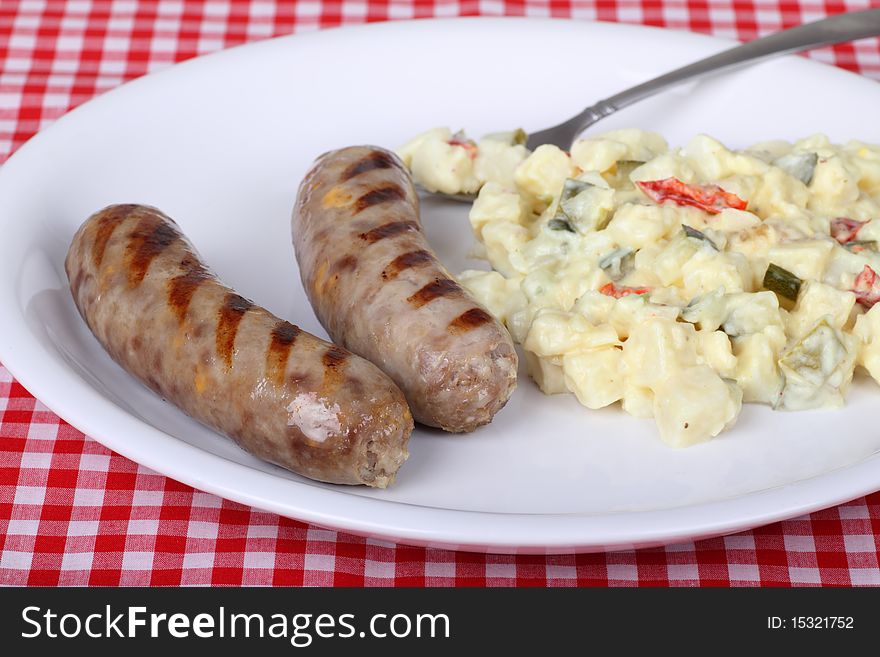 Grilled bratwurst with potato salad on a white plate