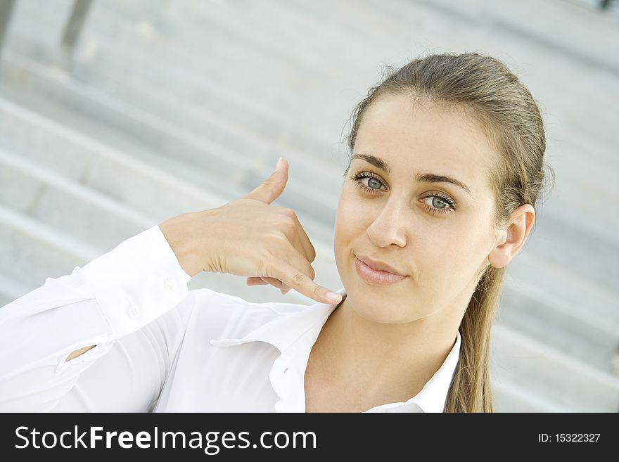 Young businesswoman outdoors on the stairs near the office building shows a sign of Call me