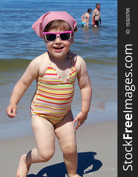 Little girl in pink glasses, runs along the beach