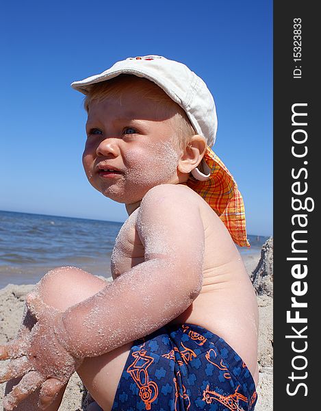 Small boy sits on beach, it is looked on sea