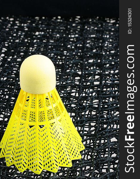 A bright yellow badminton shuttlecock on a black badminton net. A bright yellow badminton shuttlecock on a black badminton net.