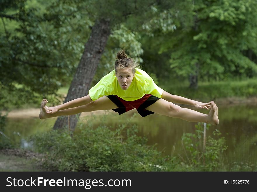 Cute young girl jumping outside in front of pond. Cute young girl jumping outside in front of pond