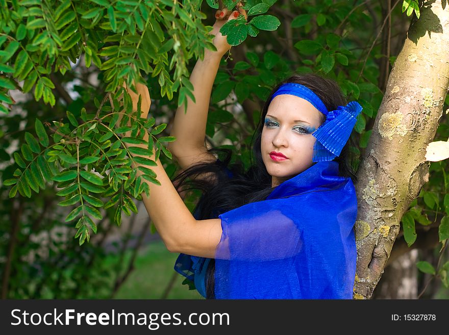 Beautiful girl with blue eyes and dark hair. Girl dressed in a blue cloth, like a dress. In her hair - burgundy flower. Beautiful girl with blue eyes and dark hair. Girl dressed in a blue cloth, like a dress. In her hair - burgundy flower
