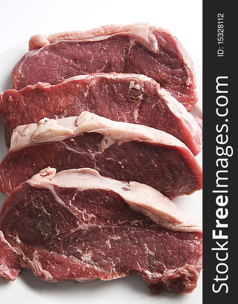 Four red raw steaks on a white plate, ready for the frying pan