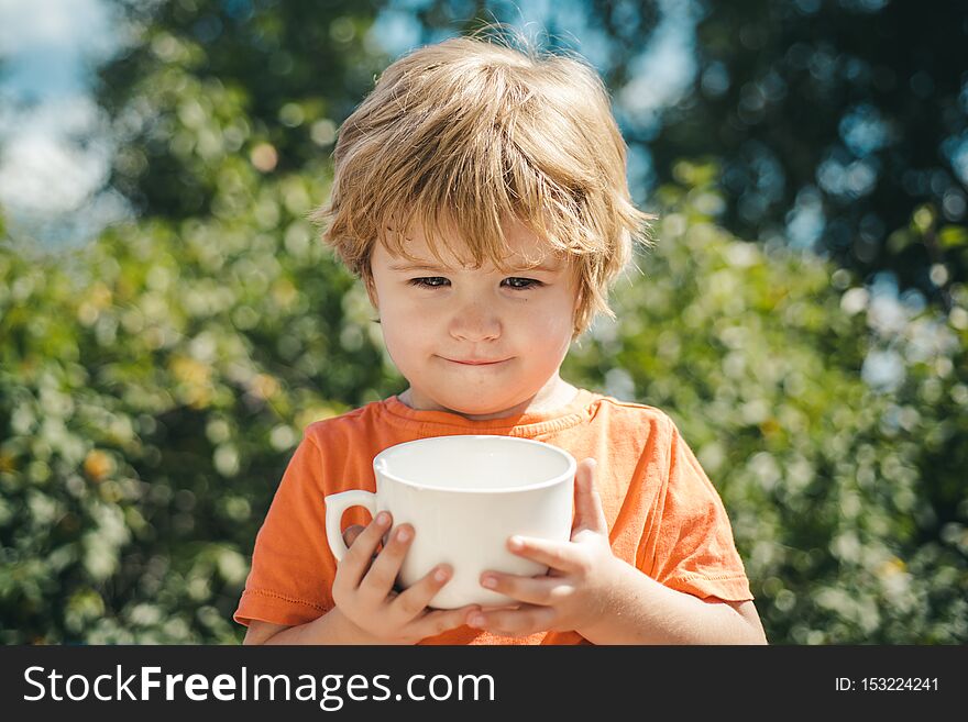 Children holidays on nature background. Drink milk with white cup. Cute child.