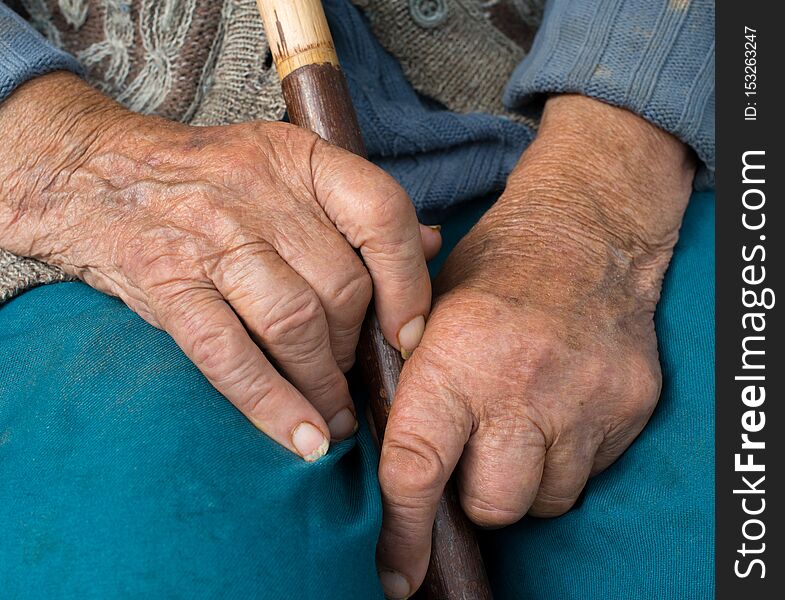 Hands of the old peasant woman. Holding the wooden walking stick