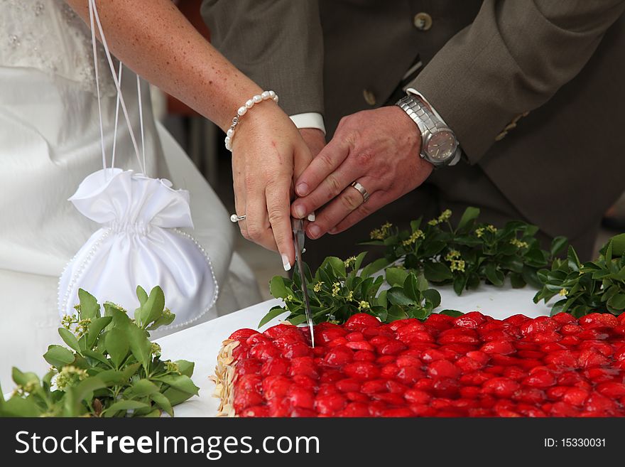 Just married couple is cutting the strawberry wedding cake.