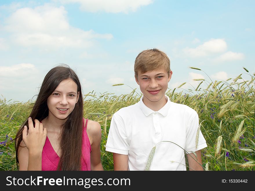 Smiling girl and boy standing in a field on background of blue sky with clouds