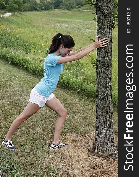 Young woman stretching on a tree before going jogging in a nature area