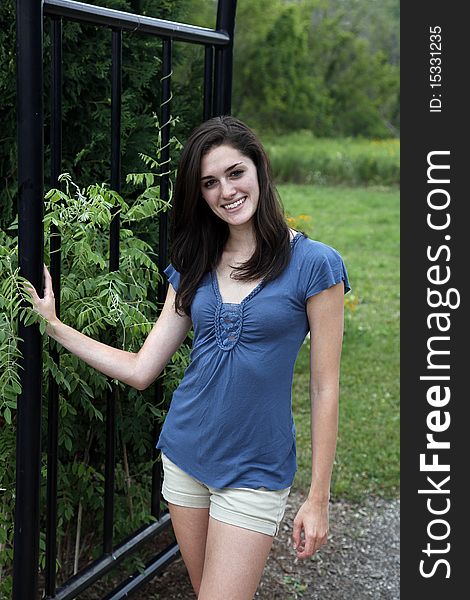 Young woman smiling beside a black wrought iron fence in a nature area. Young woman smiling beside a black wrought iron fence in a nature area