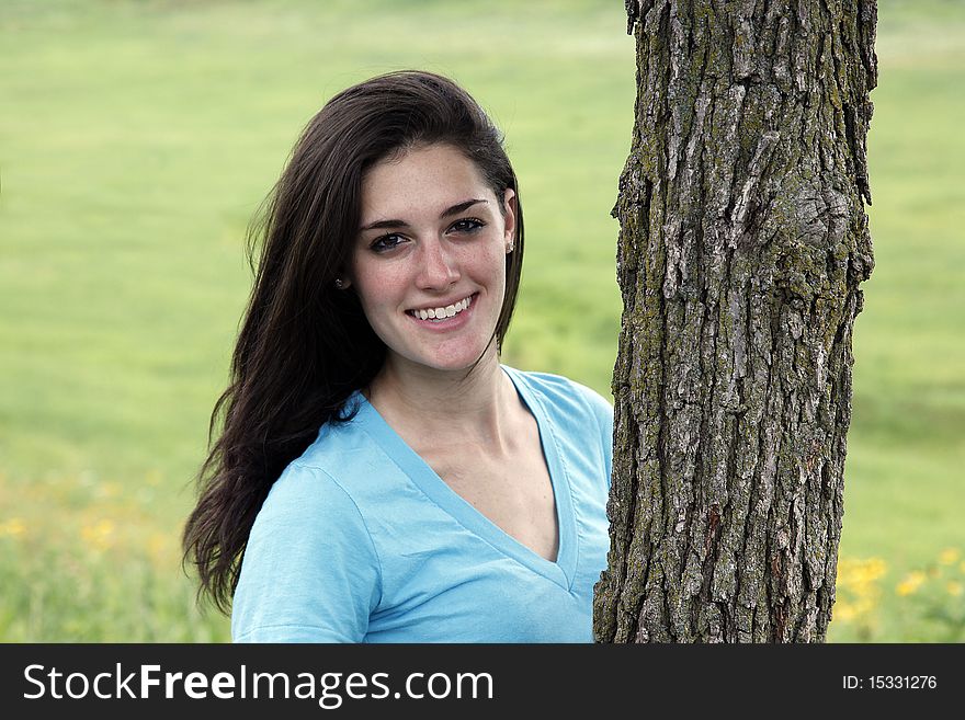 Young woman smiling beside a tree in a meadow area