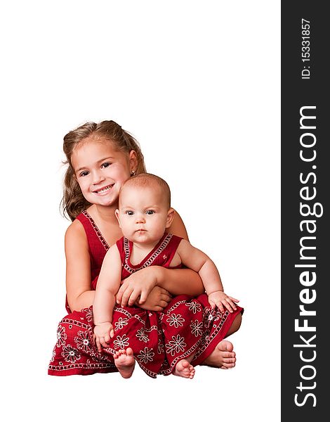 Big sister holding little sister wearing matching dresses. White background