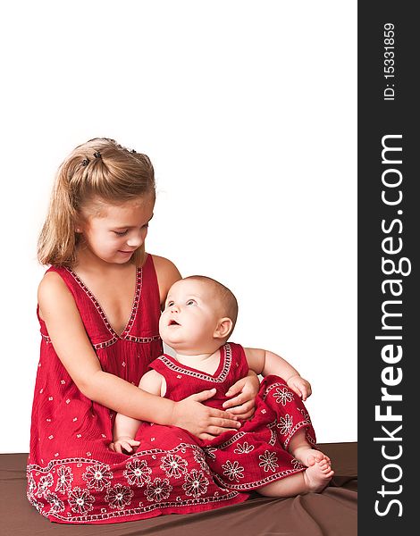 Big sister holding little sister wearing matching dresses.  White background