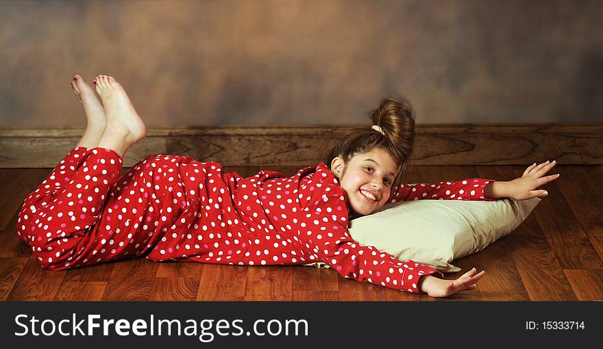 A happy preteen laying on a wood flloor with her pillow in polka-dot pajamas. A happy preteen laying on a wood flloor with her pillow in polka-dot pajamas.