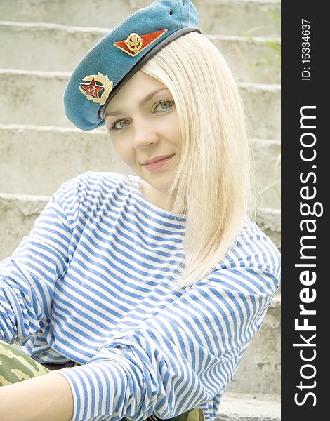 Woman with green eyes in the military form sits on a ladder. Woman with green eyes in the military form sits on a ladder