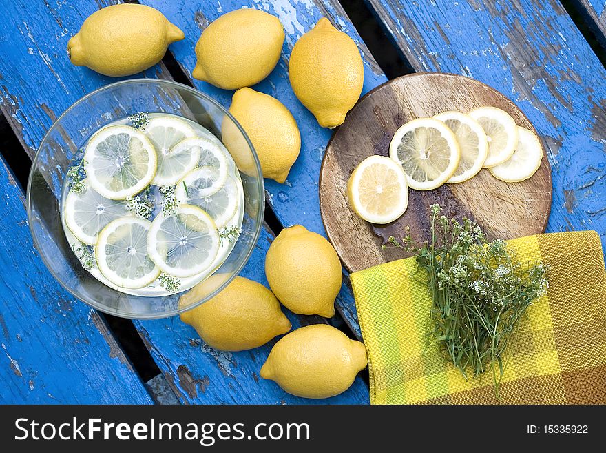 Rustic scene of lemons on old blue table. Some sliced lemons are in bowl of water.