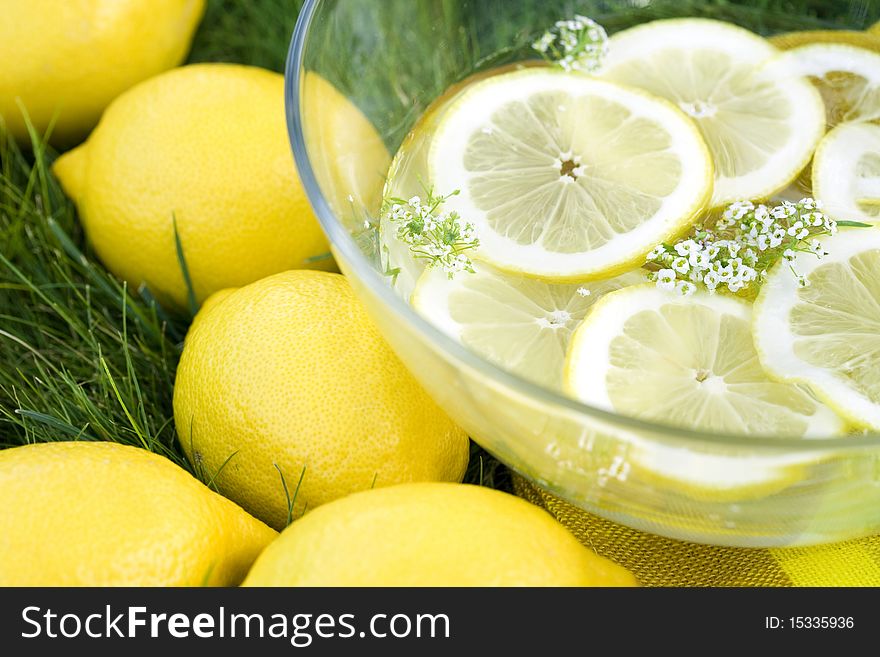 Top view of fresh lemons on a grass and sliced lemons in bowl of water