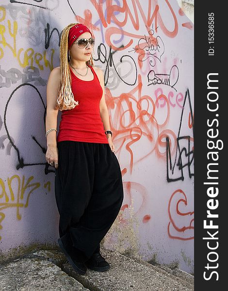 Hip-hop chick posing at the graffiti sprayed wall outdoors. Hip-hop chick posing at the graffiti sprayed wall outdoors