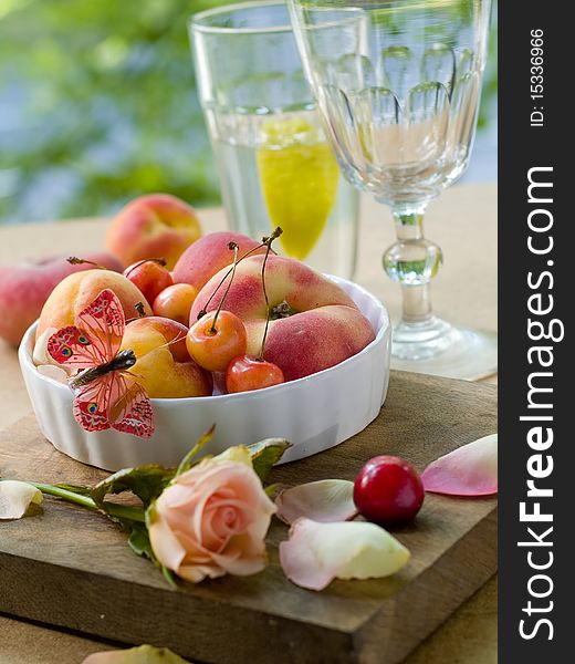 Fresh apricots, plums, cherry in bowl with butterfly rose on foreground. Fresh apricots, plums, cherry in bowl with butterfly rose on foreground