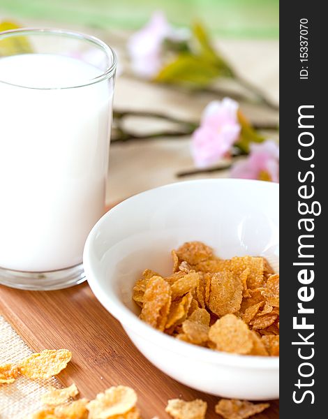 Cornflakes in a white bowl with milk in a glass on a table. Cornflakes in a white bowl with milk in a glass on a table
