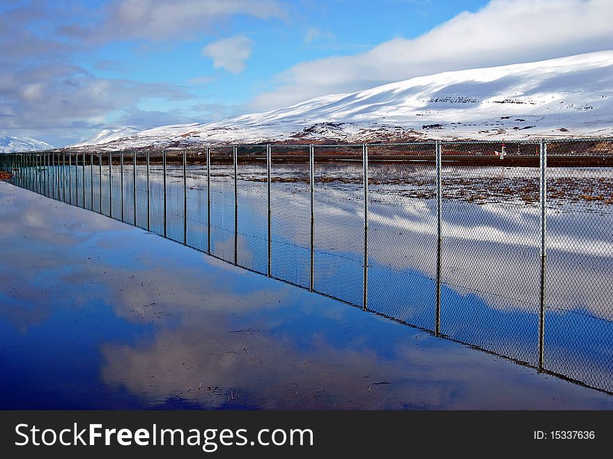 A fence and a blue sky mirrors in a water. A fence and a blue sky mirrors in a water.