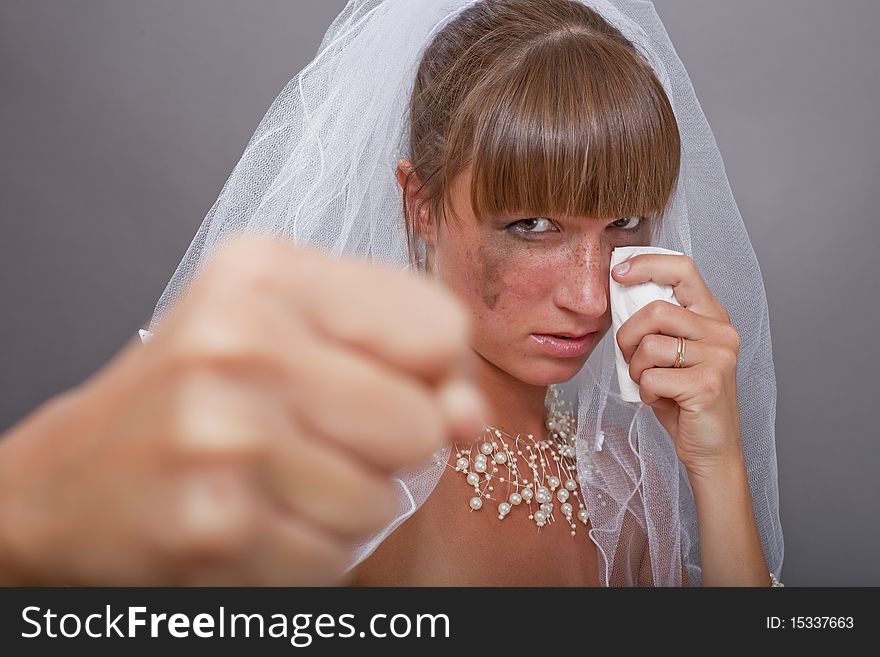 Frustrated bride punching in the camera over grey background