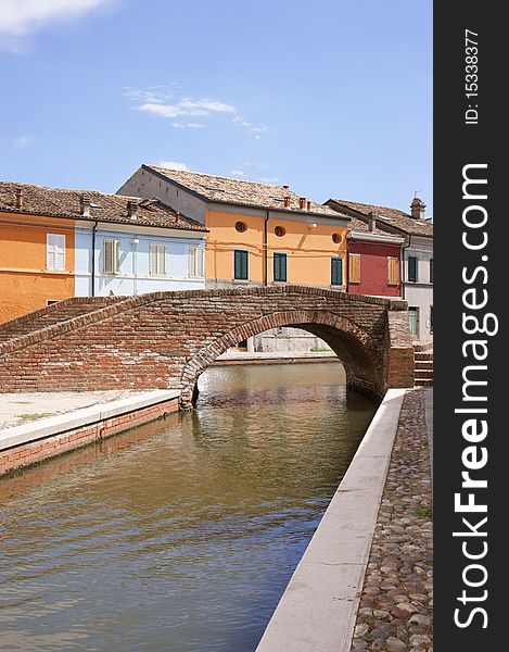 Stone arch bridge over a canal with colored houses behind