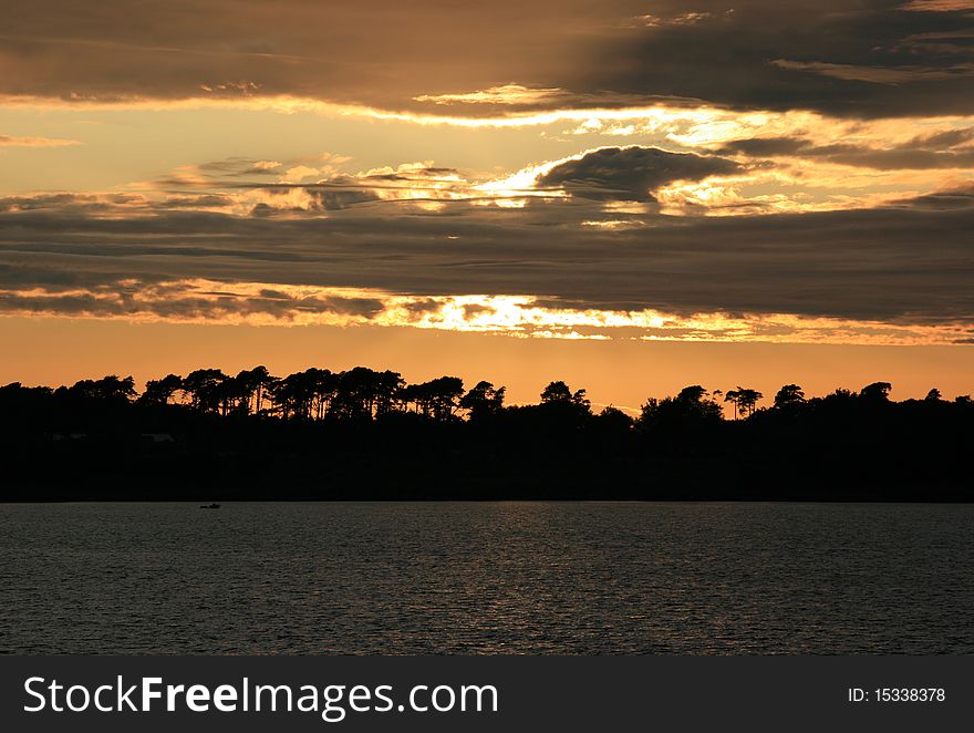Sunset over lake in Scotland with silhouette of trees in distance.