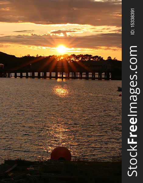Sunset over the water on the Isle of Mull in Scotland with silhouette of trees and pier in distance. Sunset over the water on the Isle of Mull in Scotland with silhouette of trees and pier in distance.