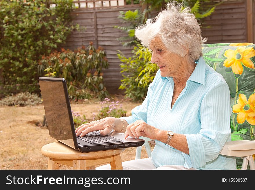 A senior woman using a laptop computer in her garden. A senior woman using a laptop computer in her garden