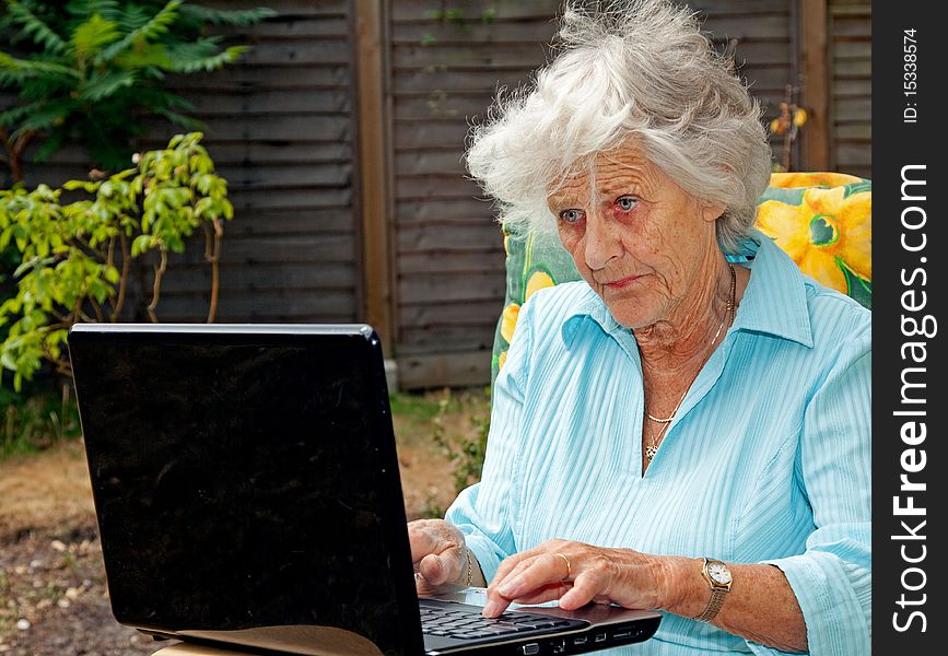 A senior woman using a laptop computer in her garden. A senior woman using a laptop computer in her garden