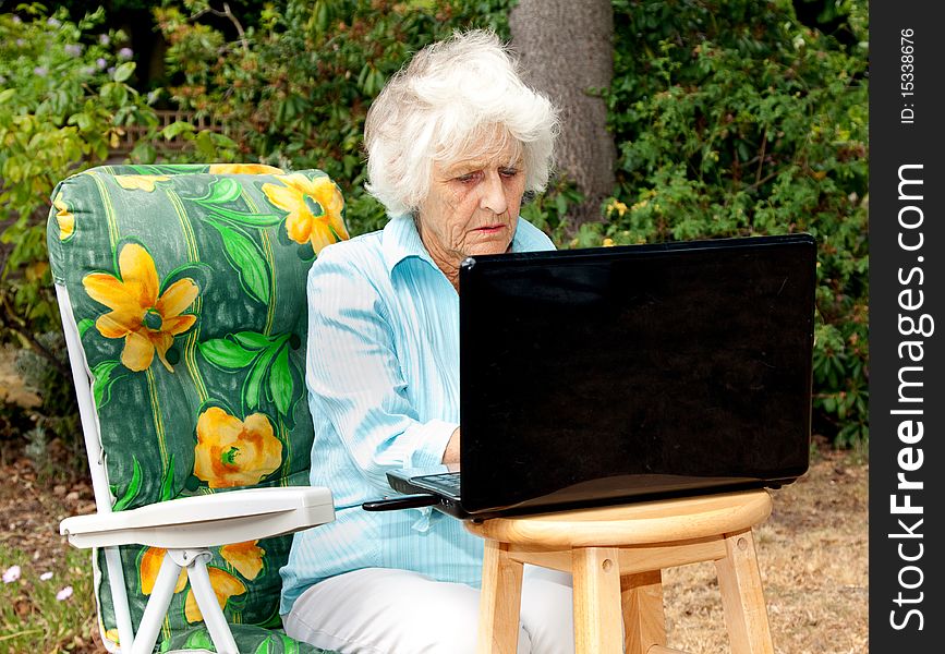 A senior woman using a laptop computer in her garden. A senior woman using a laptop computer in her garden