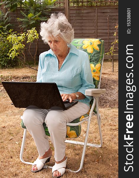 A senior woman using a laptop computer in her garden. A senior woman using a laptop computer in her garden