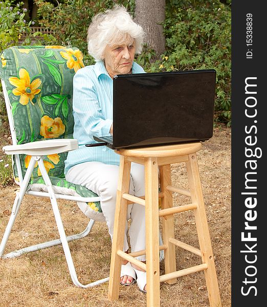 An elderly woman using a laptop computer in her garden. An elderly woman using a laptop computer in her garden