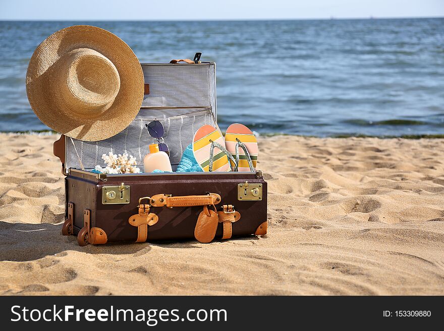 Open suitcase with stylish beach accessories on sand near sea. Space for text