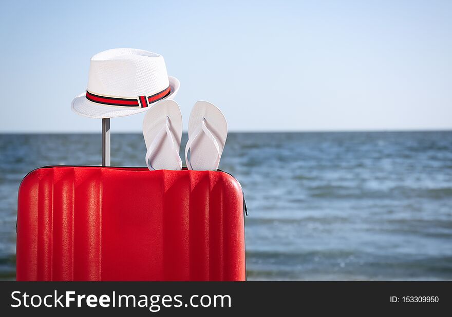 Bright suitcase and different beach accessories on sand near sea. Space for text