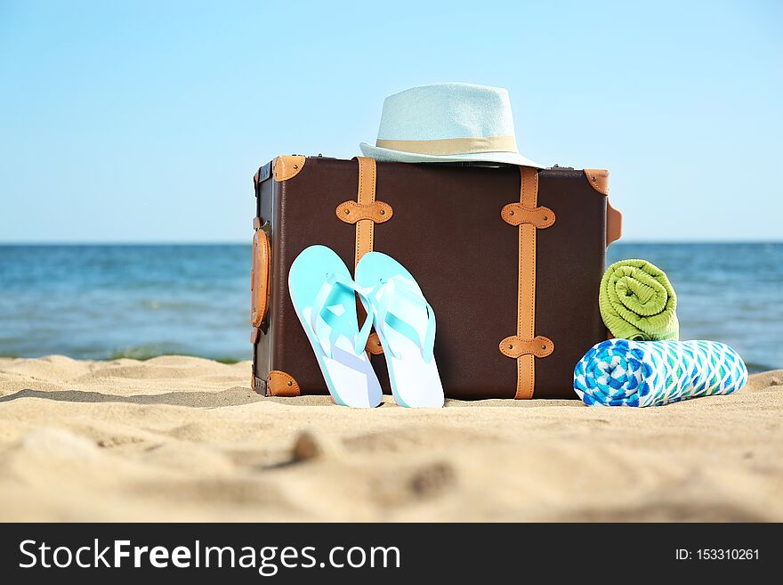 Suitcase and beach accessories on sand near sea