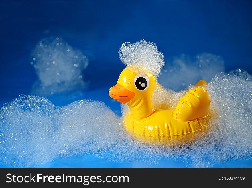 Rubber yellow duck toy on a blue background in foam. Personal hygiene