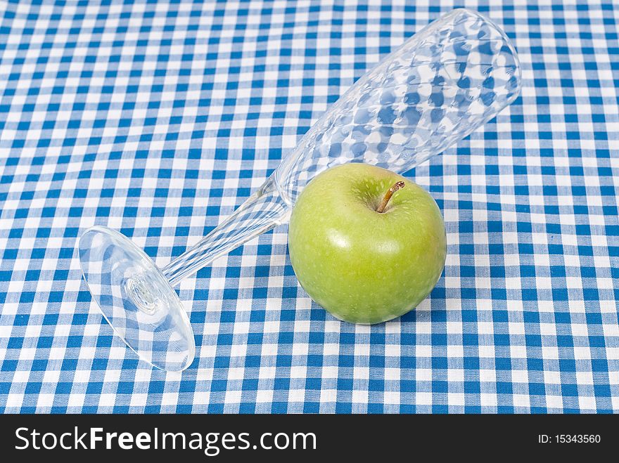A green apple with a flute glass on picnic cloth. A green apple with a flute glass on picnic cloth
